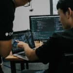 Two men working on cybersecurity on a laptop and desktop