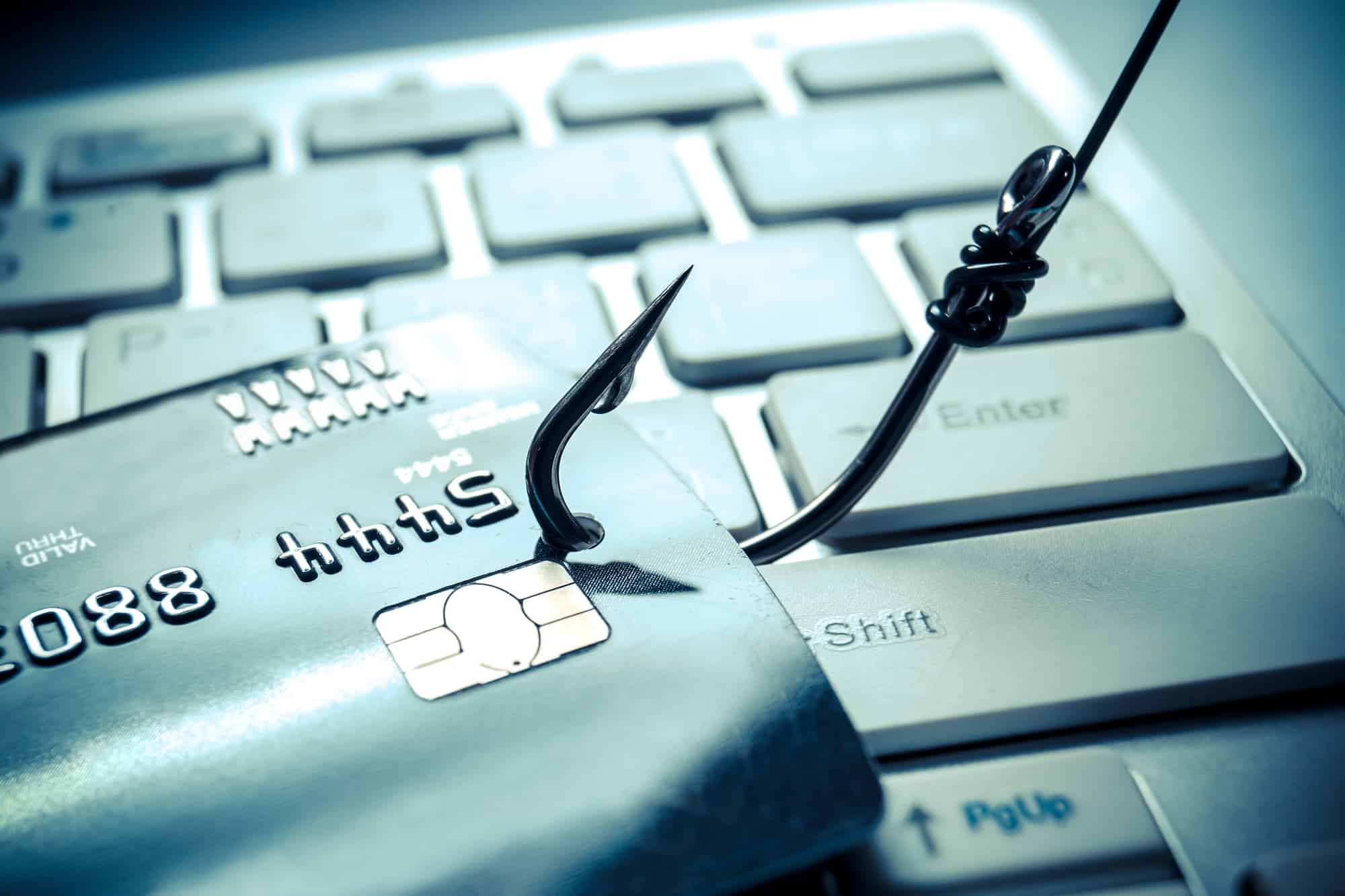 A credit card with a fishing hook through it on a keyboard.