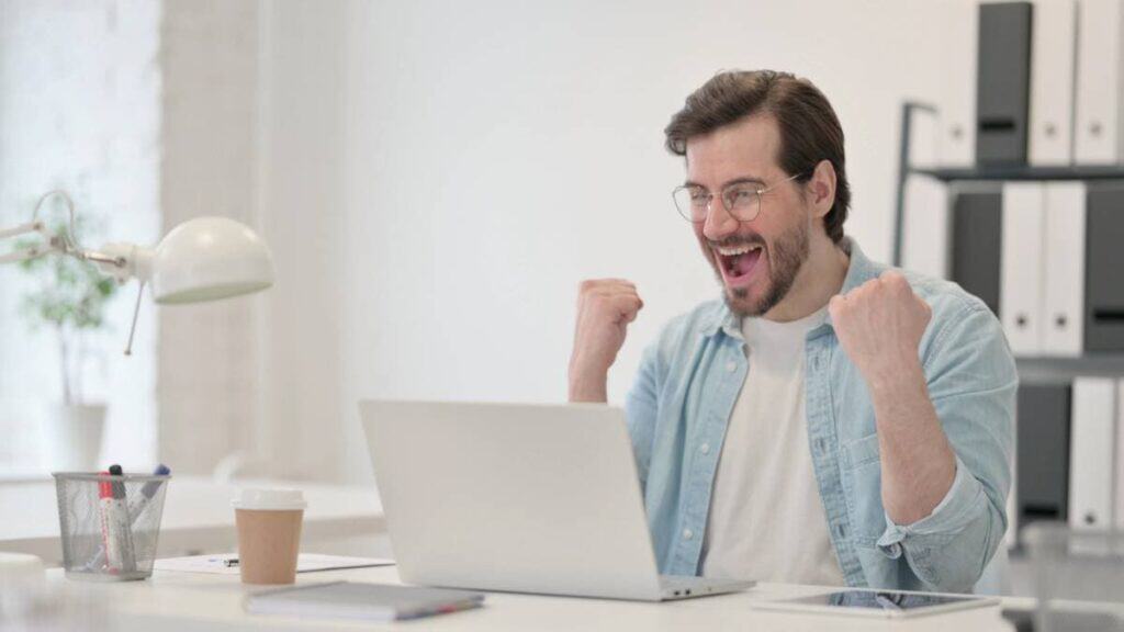 happy man in front of his laptop celebrating the results of managed IT