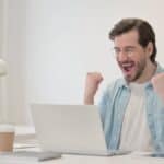 happy man in front of his laptop celebrating the results of managed IT