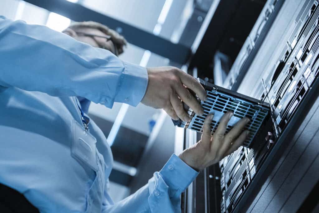 An IT technician is installing a hard drive into a server in a data center.