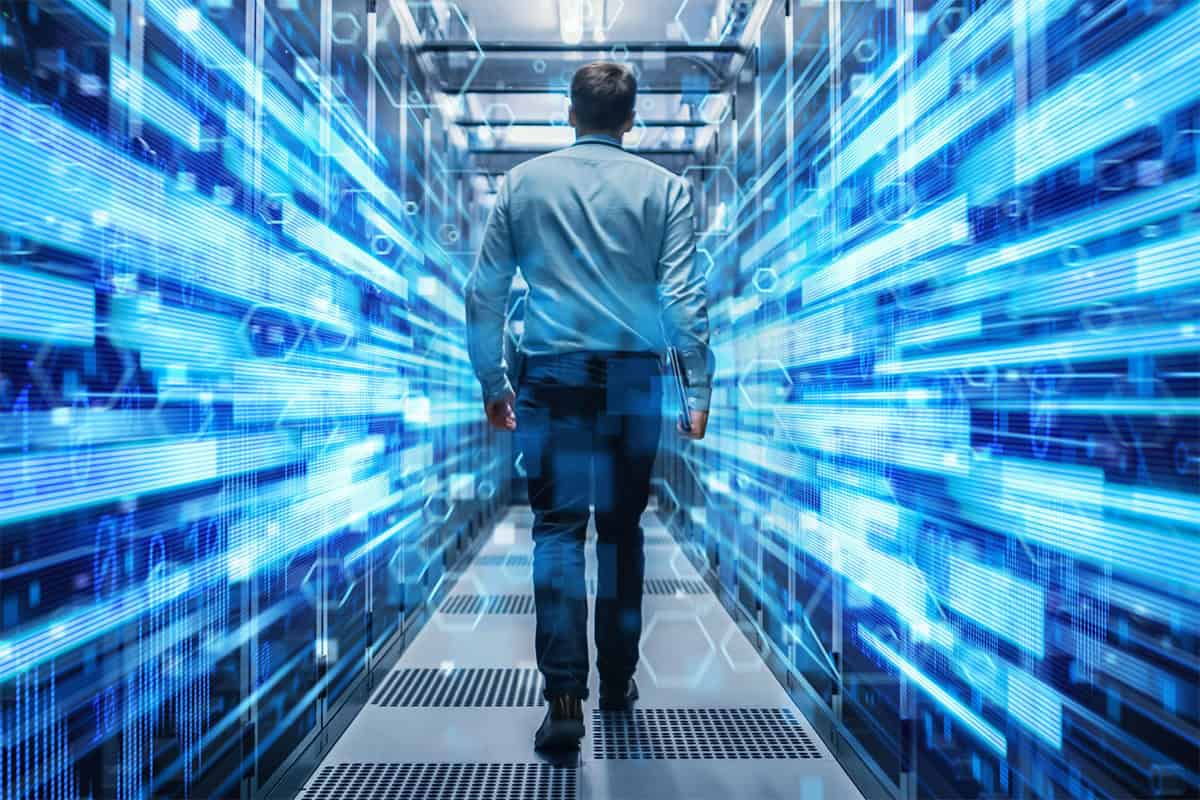 A young IT specialist is walking through a corridor in a data center full of rack servers.