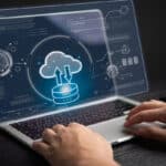 A businessman is using a laptop showing an icon of a data server uploading to a cloud.