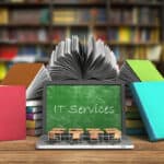 IT Services for Education A laptop is on a desk surrounded by books. The screen is showing a green chalkboard with the text "IT Services" written in chalk.
