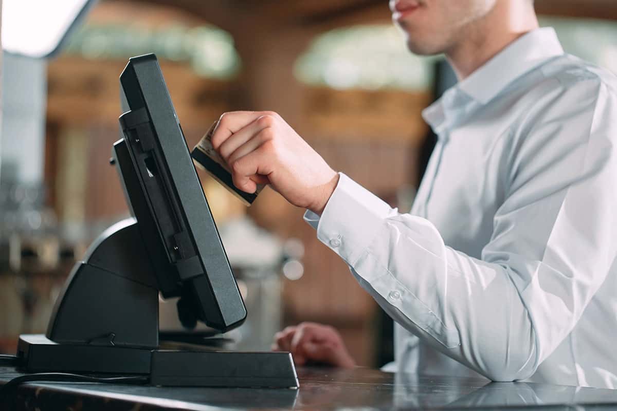 A server wearing a white dress shirt is swiping a credit card through a POS system in a restaurant environment.